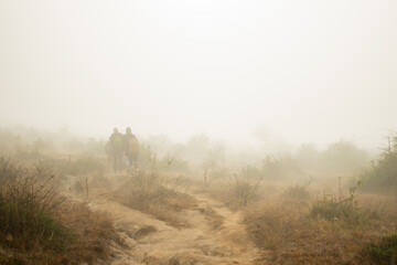 People walking in heavy early mist on trail, Myanmar