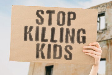 The phrase " Stop killing kids " on a banner in hand with blurred background. Violence. Death. Children. Killed. Strikes. Rockets. Bombing. Ruined. Life. Attack. Battle