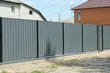 a long gray metal wall of a private fence and a closed door on a rural street