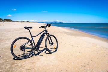un vélo à assistance électrique sur une plage de sable blanc avec une mer bleue - obrazy, fototapety, plakaty