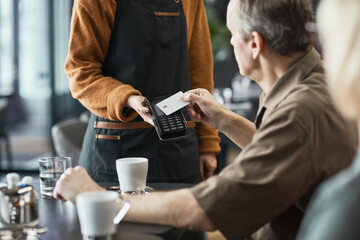 Senior man using contactless card while paying for bill through terminal with NFC in cafe