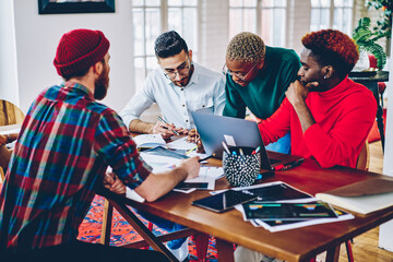 Multicultural team of male and female designers collaborating on startup project having...