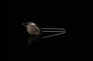 Metal sieve with a handle on black background with reflection