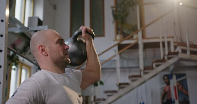 Paralympian man with defective legs looking at the camera sitting in a wheelchair training in the gym lifts a heavy weight trains his arms inside