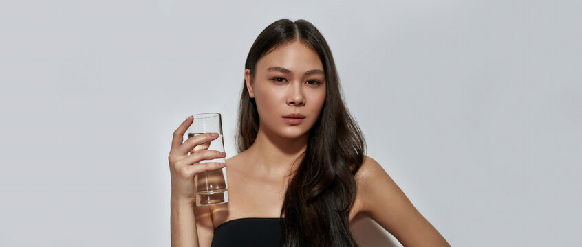 Cute young asian woman holding glass with water