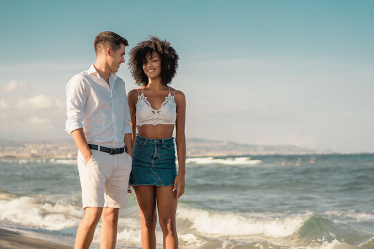 Romantic interracial couple having fun outdoors on the beach walking and talking together