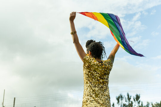 Mujer transgénero de espaldas sosteniendo bandera LGTBQ 