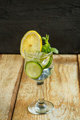 Cocktail cucumber water with lemon and mint in a glass on a wooden table on a black background.