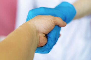 Handshake with the Doctor. The doctor's hand in a blue latex glove holds the patient's hand in close-up. Shake hands. The concept of care, trust, protection, care and support. Medicine and healthcare