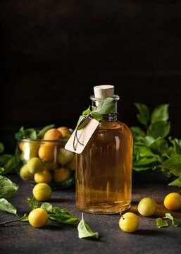 A glass bottle of delicious yellow plum liqueur or wine on wooden table. Homemade strong alcoholic beverage. Dark rustic style.