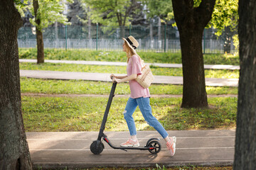 attractive girl in straw hat with scooter in the park on a summer walk