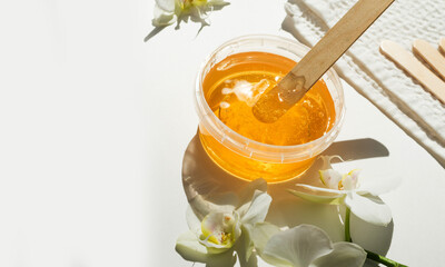 Sugar paste or wax honey in a transparent jar and white orchid on a white background. Sugaring....