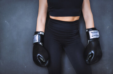 Fototapeta na wymiar the body of a boxer girl. only the trunk and arms with the gloves are visible. the leotard and gloves are black on a gray background.