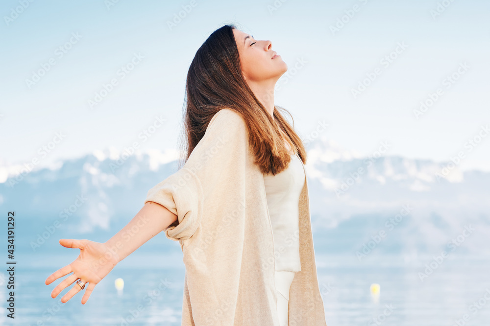 Wall mural Outdoor portrait of beautiful middle age hispanic woman enjoying nice sunny day by the mountain lake, arms wide open, breathing fresh alpine air