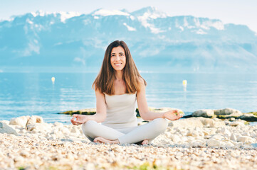 Fototapeta na wymiar Beautiful spiritual woman meditating by the lake, wearing beige clothes