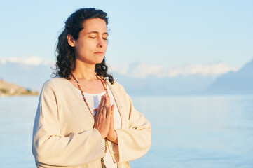 Beautiful spiritual woman meditating by the lake, wearing beige clothes