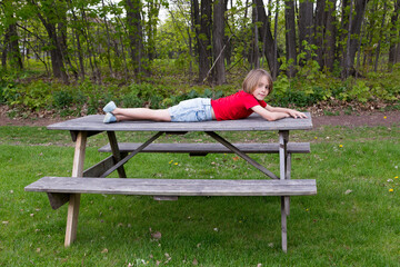 Horizontal view of cute little blond boy in casual clothes lying down on wooden picnic table