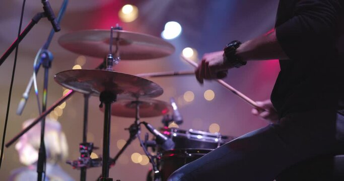 Musician drummer playing musical instrument against backdrop of bright lights. Live concert of pop band on stage. Close up of hands
