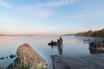 Unrecognizable men on shore of the lake geting ready for fishing. Foggy morning.