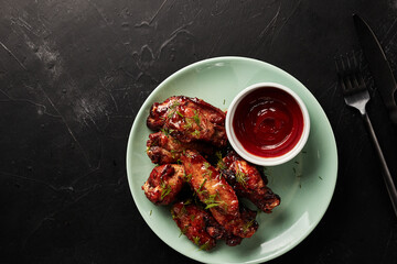 chicken wings with ketchup on a light plate on a black textured background top view