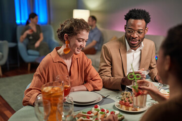 Portrait of elegant mixed-race couple enjoying dinner with friends at home and smiling, copy space