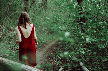 Woman in backless burgundy red dress walking on a path in the forest