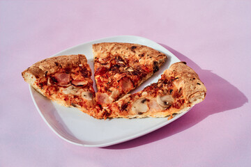 Minimalist composition of a plate with slices of pizza with hard shadow on a pink background