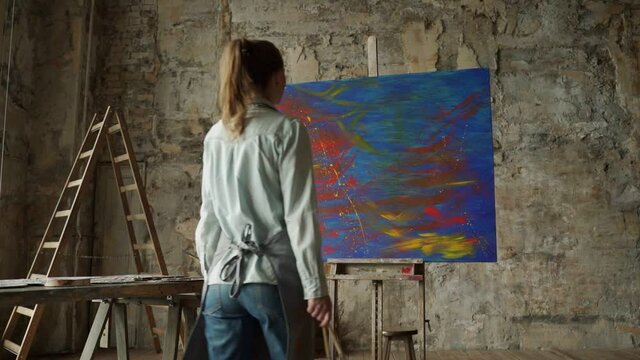 Female artist approaches an easel with a painting