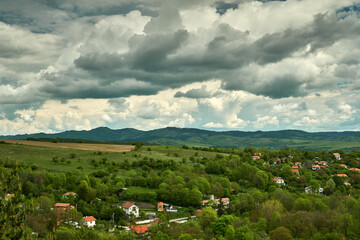 Fototapeta na wymiar A mountain village in spring, lush green fields and trees, hills and dramatic clouds