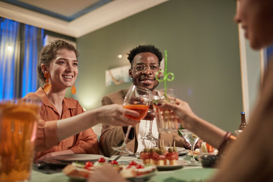 Low Angle Portrait Of Elegant Mixed-race Couple Enjoying Dinner With Friends Indoors And Clinking Glasses Over Festive Table, Copy Space