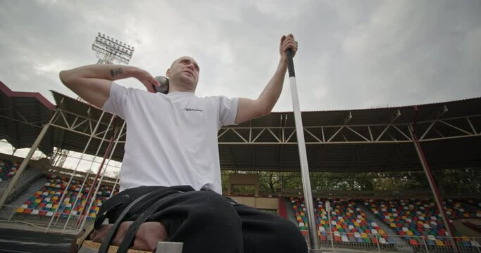 Throwing a kettlebell with his hand at a distance Paralympic strong-spirited man with defective non-working legs in a wheelchair, performing the throwing exercise sitting on a special mount