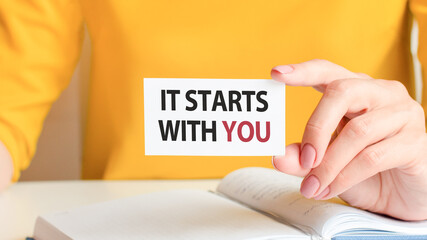 text it starts with you written on a white paper card in woman hand, concept