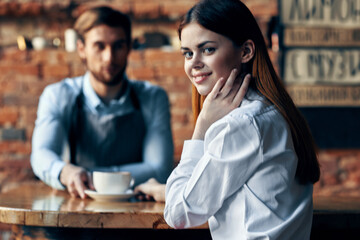 happy woman with a cup of coffee and male bartender in the apron at the table indoors