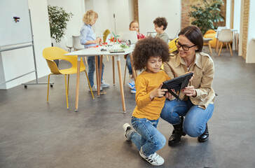 Full length shot of kind young female teacher smiling while showing video on tablet pc to her...