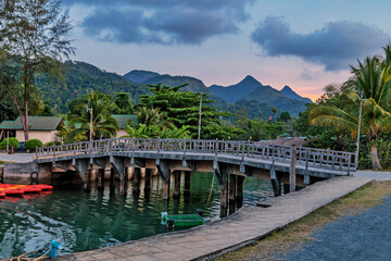 Bridge over small river in sunset on mountains background.