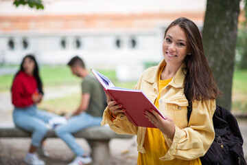 Fototapeta premium Woman student holding a book in front a a group of friends