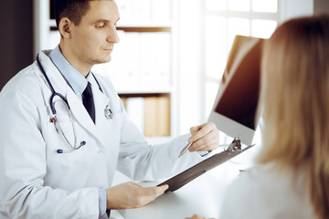 Friendly male doctor and patient woman discussing current health examination while sitting in sunny...