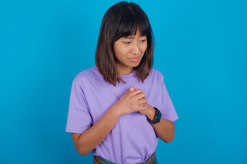 Sad young beautiful asian woman wearing purple t-shirt against blue wall desperate and depressed with tears on her eyes suffering pain and depression  in sadness facial expression and emotion concept