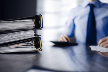 Binders with papers are waiting to be processed by man accountant in blue shirt staying at home...
