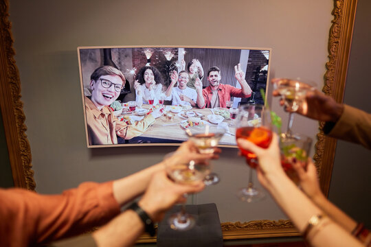 Close up of unrecognizable group of people clinking glasses to screen while celebrating online with friends