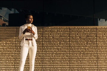 Outdoor portrait of a young black African American woman using a cell phone. Beautiful African woman standing communicating with friends. Technology concept