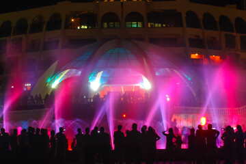People looking at fountain musical performance at night against casino. C