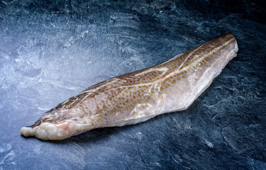 Fototapeta premium Roher norwegisches Skrei Kabeljau Fisch Filet mit Haut angeboten als close-up auf einem schwarzen Board mit Textfreiraum