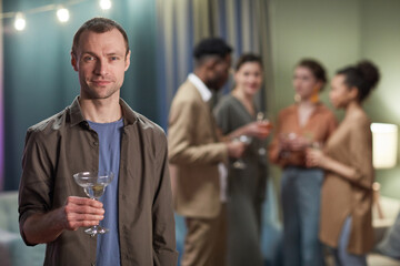 Waist up portrait of adult man looking at camera and holding cocktail glass while enjoying party at home, copy space