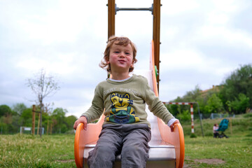 Cute happy little boy playing on slide in Playground Outdoors