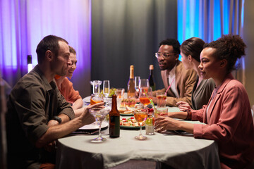 Side view at diverse group of young people at dinner table laughing happily while enjoying party indoors