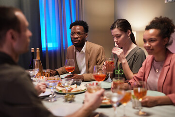 Diverse group of young people sitting at dinner table while enjoying party indoors