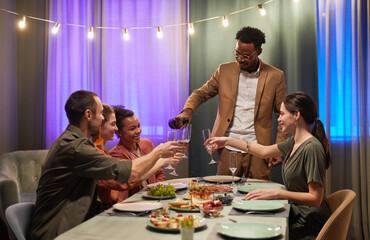 Portrait of African-American man pouring wine to glasses while enjoying dinner party with friends
