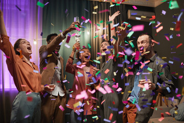 Obraz na płótnie Canvas Diverse group of excited young people dancing under confetti shower while enjoying party with friends indoors