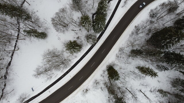 Füssen, Germany Bavaria - February 16, 2021: Striped paved winter road winding through the snowy forest trees with a bike path and silver car. Image taken from a drone at 100m altitude. Background.
